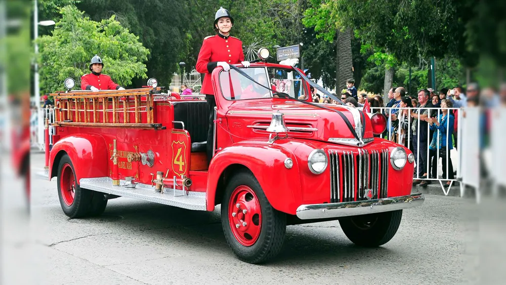 La 4-A, carro bomba Ford de 1946, desfila con dos bomberos de la Cuarta de pie en dolman rojo y casco.