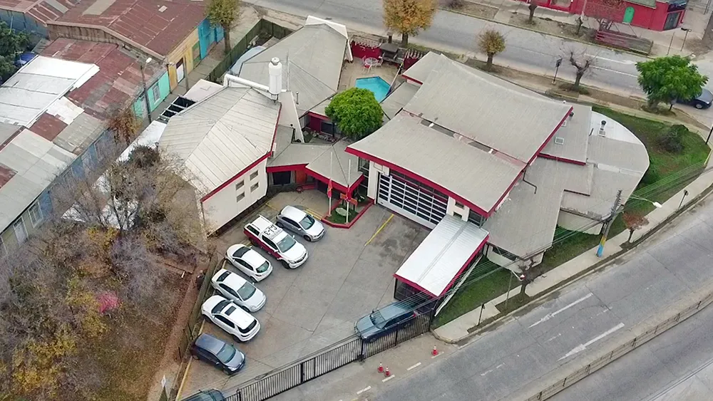 Vista aérea del cuartel de la Cuarta en Quillota esquina 12 Norte: techos grises con filetes rojos y el patio de estacionamiento.